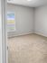 Bright and airy empty room with plush carpeting and a large window offering views of the blue sky.