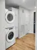 Modern laundry room featuring stackable washer and dryer with elegant white cabinetry and hardwood flooring.