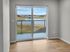 Bright room with hardwood floors and sliding glass doors opening to a scenic view of a serene lake and sprawling greenery.