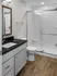 Modern bathroom featuring sleek white subway tiles, a spacious glass-enclosed shower, elegant vanity with a dark countertop, and warm wood flooring.