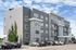 Modern apartment building exterior with sleek gray siding, multiple balconies, and ample parking, set against a bright blue sky.