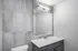 Modern bathroom with stylish gray tiles, a large mirror, and sleek vanity featuring a pristine white countertop.