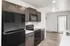 Sleek, modern kitchen with dark cabinetry, stainless steel appliances, and wood flooring, leading to a bright entryway.