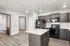 Modern kitchen with dark cabinetry, sleek appliances, and an island, adjacent to a bathroom, highlighted by elegant wood flooring.