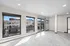 Bright modern apartment living area featuring large windows, sliding glass doors, and sleek flooring with city views.