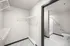 Spacious walk-in closet with ample shelving leading into a modern bathroom featuring a sleek shower and pristine white fixtures.