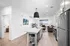 Modern open-concept kitchen and living room with sleek finishes, featuring a cozy sofa, vibrant artwork, and large window with city view.