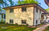 Charming two-story duplex with classic white siding, nestled in a serene neighborhood with lush greenery.