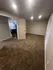 Spacious carpeted room with modern lighting, open doorway leading to a kitchen area.