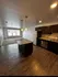 Modern open-concept kitchen with granite countertops, stylish pendant lighting, and sleek stainless steel appliances, leading into a spacious, well-lit living area with large windows.