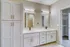 Elegant bathroom featuring double sinks, sleek cabinetry, and bright lighting next to a walk-in closet.