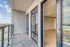 Modern balcony with glass railing offering a serene view, seamlessly connected to a spacious living area with elegant hardwood flooring.