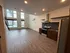 Bright and modern living space with high ceilings, large windows offering city views, sleek kitchen with stainless steel appliances, and stylish wooden flooring.