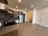 Modern kitchen area with stainless steel appliances, sleek countertops, and wooden cabinets, leading into a spacious, open-concept living space with hardwood flooring.
