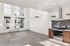 Modern open-concept apartment with high ceilings, large windows, and a sleek kitchen featuring stainless steel appliances.
