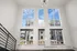 Bright, open loft space featuring large floor-to-ceiling windows with a scenic city view, modern chandelier, and sleek railing.
