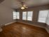 Bright and inviting room with polished hardwood floors, ample natural light from multiple windows, and a modern ceiling fan.