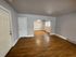 Charming living space featuring elegant hardwood floors, arched doorway leading to a well-lit dining area, and ample natural light from large windows.