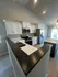 Modern kitchen featuring sleek white cabinetry, stainless steel appliances, and a spacious breakfast bar with recessed lighting.