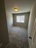 Cozy, carpeted room with soft lighting and a bright window view, ideal as a small bedroom or home office.