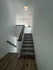 Inviting staircase with modern wooden railing leading to a bright open-plan living area with sleek lighting.