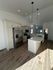Bright and modern kitchen with stainless steel appliances, elegant lighting, and spacious island on hardwood floors.