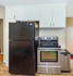 Cozy kitchen featuring stainless steel oven, spacious black refrigerator, and elegant white cabinets.