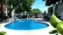 Inviting apartment complex pool area with vibrant blue waters, surrounded by lush greenery and modern lounge chairs for relaxation.