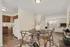 Dining area facing kitchen & living area. Kitchen & dining area have vinyl plank flooring, living room is carpeted and shows room for a couch, television set, and large window.
