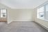 Bright, carpeted living room with large windows and neutral walls.