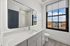 Bright and modern bathroom with a sleek marble countertop, large mirror, and stunning city view from the window.