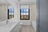 Bright, modern bathroom with a large window offering a scenic city view, sleek vanity with white countertop, and an inviting bathtub.
