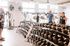 Modern fitness center with a variety of dumbbells and cardio machines, featuring large windows and a vibrant atmosphere.