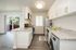 Pet-Friendly Apartments in Concord, CA - Diablo View and Villa Diablo - Modern Aisle-Style Kitchen with White Cabinetry, Stainless Steel Appliances, Light Granite Countertops, Window, Wood-Style Flooring, Laundry Machine, and a View of the Balcony
