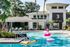 1800 The Ivy, exterior, sparkling blue swimming pool, club house entrance, lounge chairs, pink blow up flamingo, water toys, sign 'The Ivy' on side of gray and white building, trees,