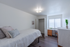 Bright, cozy bedroom with elegant wood flooring, a comfortable bed with stylish pillows, ample closet space, and a sunlit window beside a chic desk and dresser.
