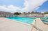 Inviting outdoor pool area with sparkling blue water, surrounded by sun loungers and a white fence, under a sunny sky. | Windmill Cove | Apartments in Sandy, Utah