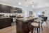 Modern open-concept kitchen with sleek dark cabinetry, granite countertops, and stylish pendant lighting, seamlessly connecting to a cozy living area with large sliding doors leading to a balcony. | Point of View | Apartments in Draper, Utah