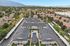 Aerial view of a serene apartment complex with modern rooftops, solar panels, lush greenery, and a central swimming pool, nestled in a picturesque neighborhood with mountain backdrop.