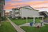 Charming apartment exterior with stone facades, lush green lawns, and a cozy pergola under a vibrant sunset sky.