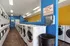 Modern communal laundry room equipped with rows of washers and dryers, featuring vibrant blue and yellow walls for a fresh and inviting atmosphere.
