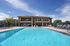 Luxurious apartment complex with a sparkling outdoor swimming pool, surrounded by elegant lounge chairs and a spacious two-story clubhouse under a clear blue sky.