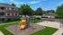 Inviting apartment complex with a vibrant playground and basketball court, surrounded by lush greenery and open space.