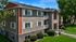 Charming apartment building with stylish brick and wood facade, surrounded by lush greenery and well-maintained lawns under a clear blue sky.