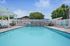 Inviting apartment pool area with bright loungers, shaded seating, and lush greenery under a clear blue sky.