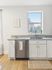 Chic kitchen featuring modern granite countertops, stylish white cabinetry, and a stainless steel dishwasher, complemented by natural light from a large window with a captivating city view.