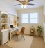 Home office. White desk and shelving unit. Brown Chair. Ceiling Fan. Carpet. Two windows.