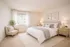Bright bedroom. Bed with white and gray linen. Chair, plant, nightstands.