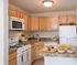 Kitchen with breakfast bar. White appliances, maple cabinetry. Pastry, orange juice, and fruit on counter.