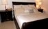 A bed with with a dark wood head board and frame and light creamy sheets sits in between two dark nightstands with lamps on them.| Houses for rent utilities included, Los Angeles, CA